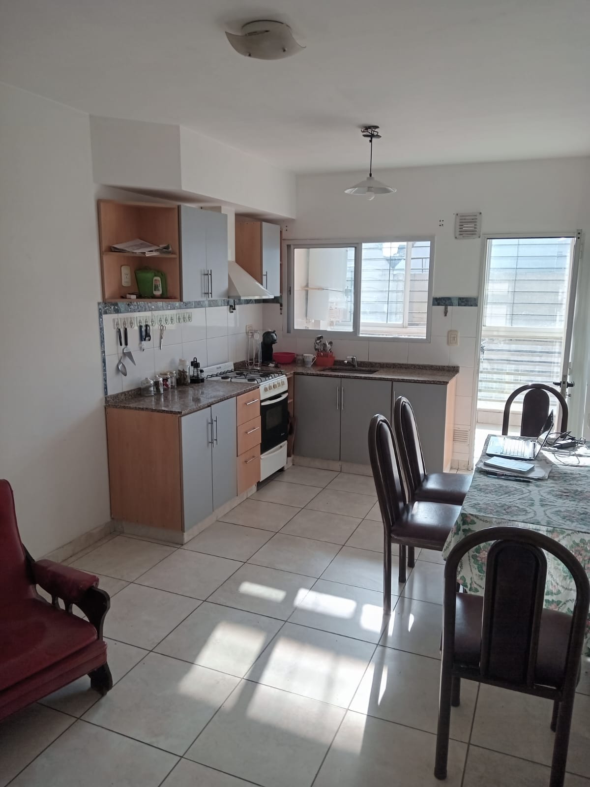 A functional kitchen area is equipped with modern appliances and ample countertop space. A wooden dining table with four chairs is positioned near a window, allowing natural light to fill the room. Shelves provide space for kitchenware, enhancing the organized setup.