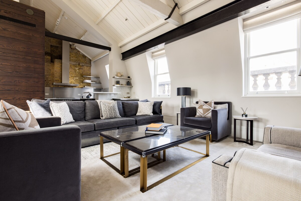 ห้องนั่งเล่นสว่างและกว้างขวางพร้อมเพดานโค้งคานเปิดโล่งและขอบอุตสาหกรรมสมัยใหม่ ที่นั่งหรูหราโทนสีกลางและเฟอร์นิเจอร์สีทองสร้างที่พักที่อบอุ่นแต่ซับซ้อนเหมาะสำหรับการพักผ่อนหรือความบันเทิงอย่างมีสไตล์