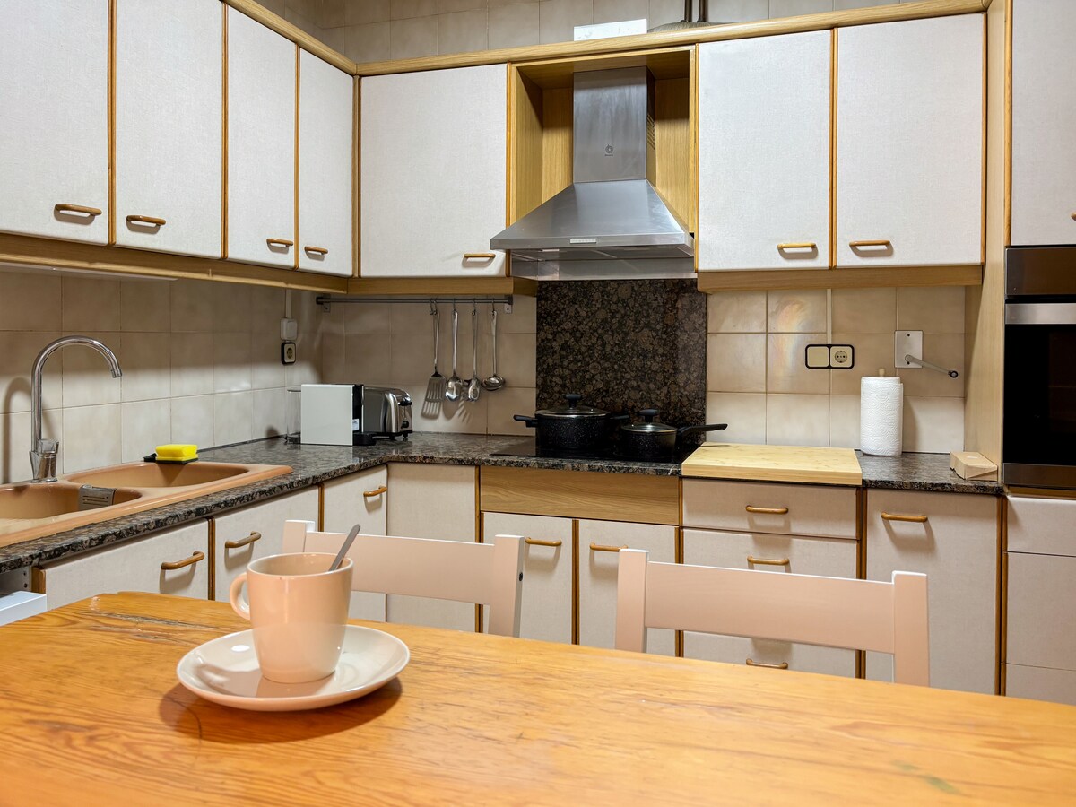 A functional kitchen is equipped with a variety of appliances, including a microwave and stove. Light wood cabinetry and a dark granite countertop provide contrast. The dining table, set with a cup and plate, emphasizes a casual dining space conducive to meal preparation and sharing.