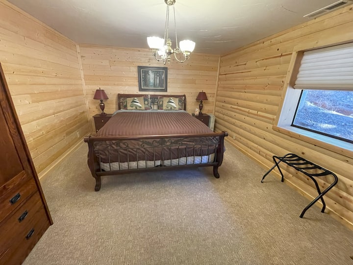 Cómodo dormitorio con una cama tamaño king y paredes rústicas de madera para una sensación de cabaña en el sótano.