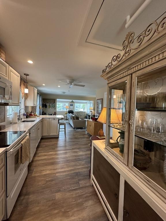 The kitchen area features modern cabinetry and stainless steel appliances along one side, with a decorative cabinet showcasing glassware on the other. Open sightlines lead to a bright living space, illuminated by natural light from large windows, enhancing the inviting atmosphere.
