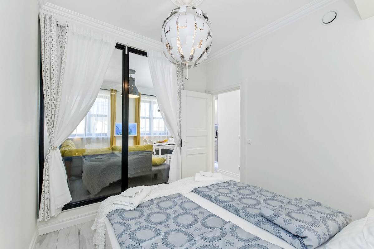 Спалня с двойно легло (ширина 160 см). Изглед към всекидневната през стъклена стена. Стъклото може да бъде затъмнено / уединението е направено с щори и завеси.