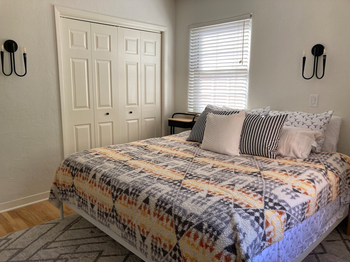 تحتوي غرفة النوم المريحة هذه على سرير كبير الحجم ووسائد متنوعة ومروحة سقف. هناك خزانة بيضاء مع تلفزيون 65بوصة وشمعدانات حائط بسيطة وستائر ذات لون فاتح. تتصل الغرفة بحمام، بتصميم محايد وبسيط.