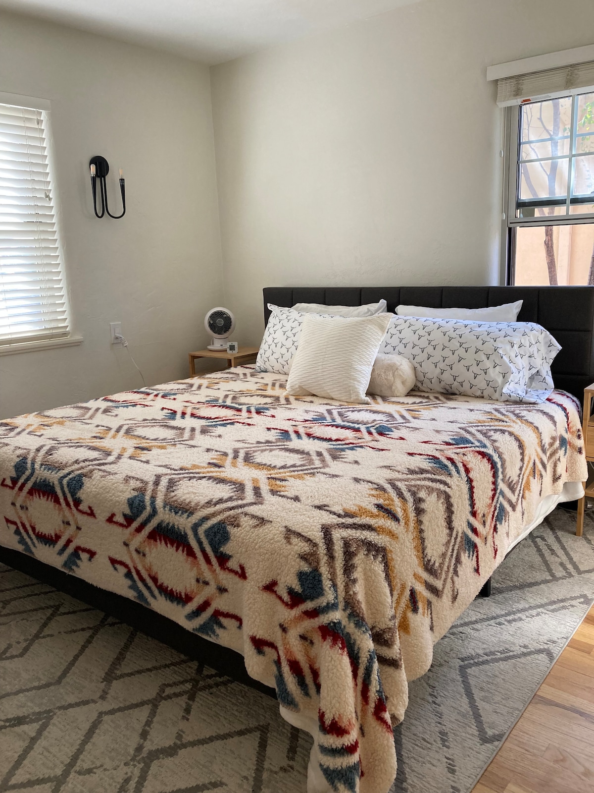 تحتوي غرفة النوم هذه على سرير كبير وجدران فاتحة اللون وضوء طبيعي من نافذتين. تضيف خزانة من الخيزران وتلفزيون على وحدة تحكم بيضاء وطاولات طرفية وظائف، بينما تعزز مروحة السقف الجو المتجدد الهواء. التصميم مريح.