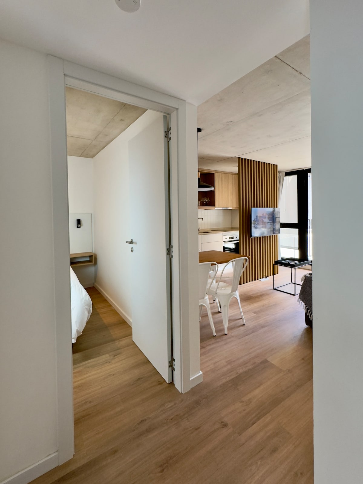 A welcoming entrance is visible, leading to a bright living space. The image shows a partially open door with sleek white walls and warm wood flooring. A glimpse of the kitchen and dining area can be seen, enhancing the open and contemporary layout.