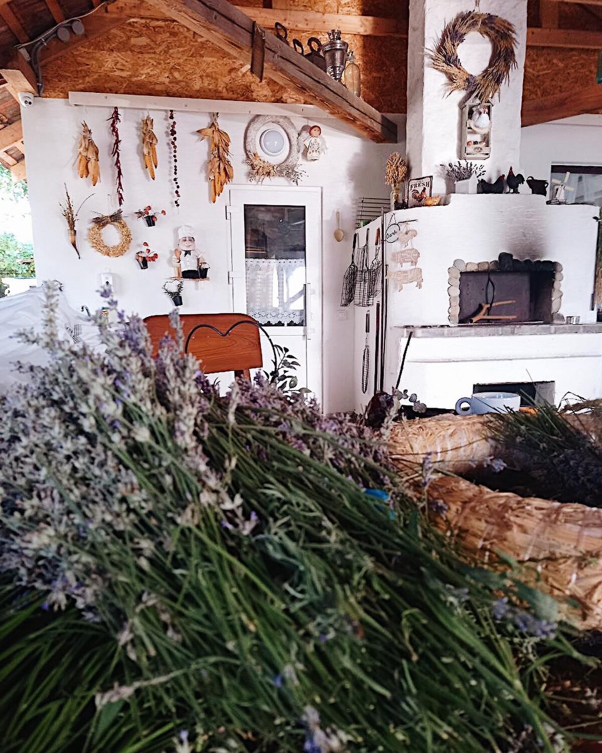 A charming interior space featuring rustic decor, including dried flowers and woven baskets. A fireplace is visible, along with various hanging decorations on the walls. Soft natural light enters through a nearby window, enhancing the inviting and cozy atmosphere.