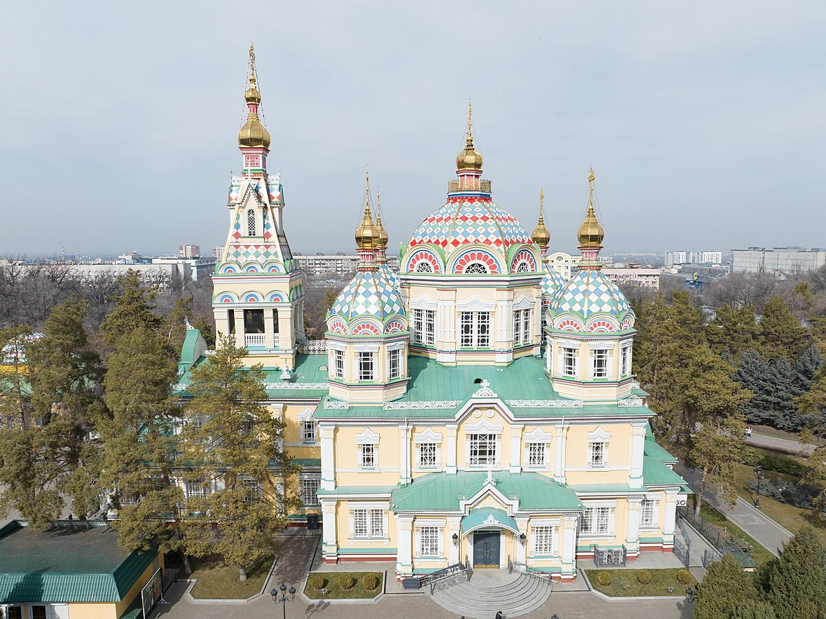The image captures an ornate building with colorful onion-shaped domes and intricate architectural details. The structure features multiple spires and a broad front, surrounded by trees, creating a welcoming presence. A clear sky serves as the backdrop, enhancing the vibrancy of the building's colors.