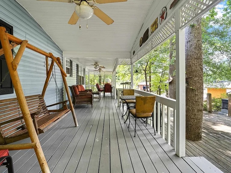 A spacious covered porch features a wooden swing and various seating arrangements. The area is surrounded by greenery, with ceiling fans providing comfort. Natural light filters through the space, highlighting the inviting layout and family-friendly atmosphere.