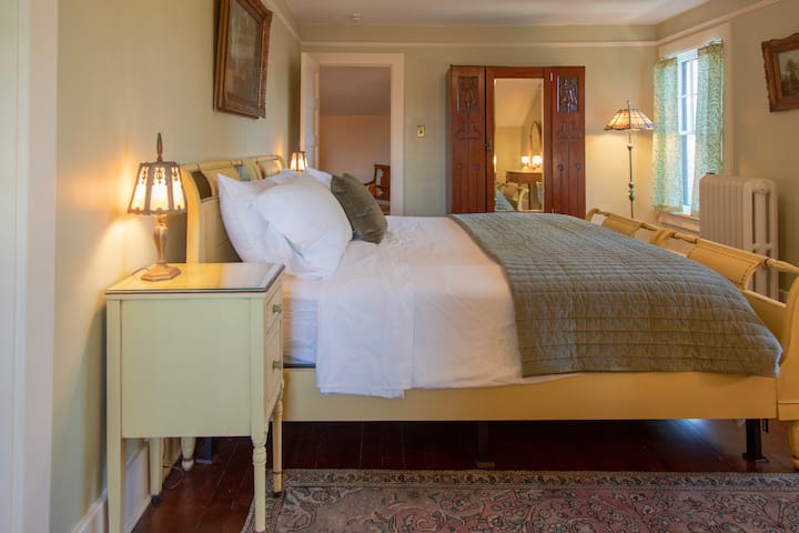 Mwonekano kutoka mbele ya sehemu ya kusoma kuelekea armoire na kitanda cha mfalme. Nguo hutoa viango na nafasi ya rafu kwa ajili ya kuhifadhi nguo. Chumba hicho kina fanicha zilizopakwa rangi kwa mkono na motif za William & Morris 'willow bough'.