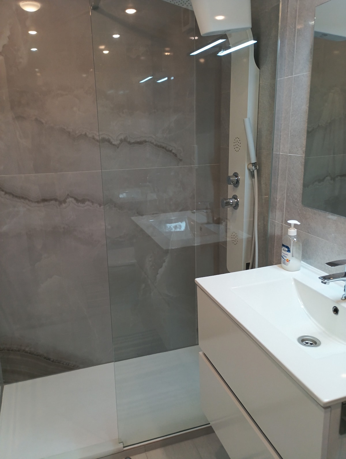 A modern bathroom is showcased with a spacious walk-in shower featuring a glass enclosure. The sleek vanity includes a white sink and storage underneath, while subtle lighting enhances the contemporary design.