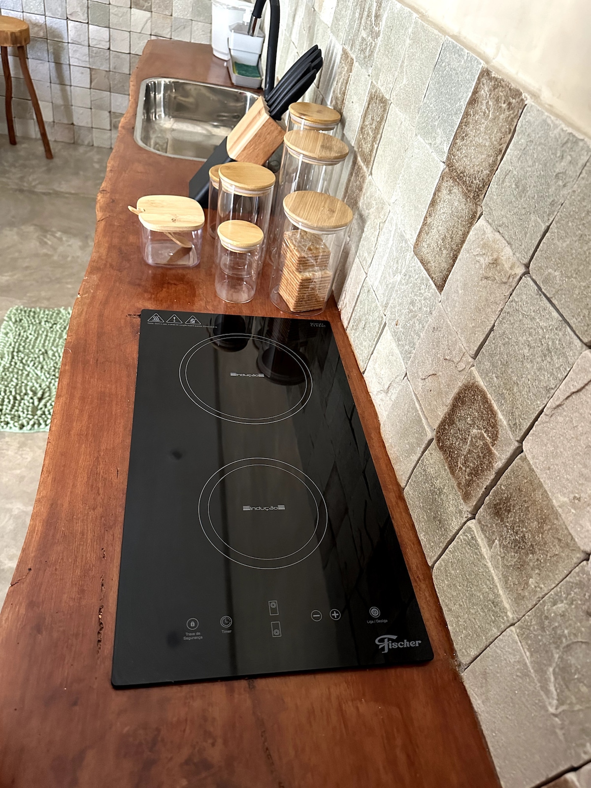 A functional kitchen area is showcased featuring an induction cooktop set atop a wooden counter. Clear glass containers with bamboo lids hold various ingredients, and an elegant sink is positioned nearby. Tiled backsplash adds a textured element to the inviting space.