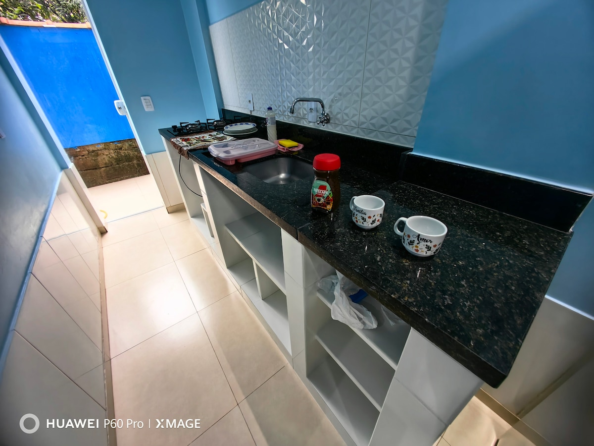A modern kitchen space is visible, featuring a dark granite countertop with a double sink. A stove is neatly arranged along the back wall. Two decorative cups sit on the counter. Cabinets below provide storage, and blue walls add a bright touch.