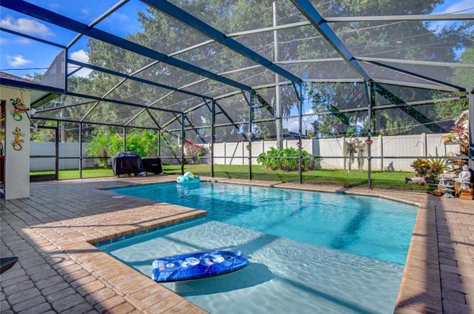A tranquil saltwater pool area features a screened lanai surrounded by landscaping. The pool is accented by a spacious patio, which includes seating and a vibrant lounging float. Sunlight filters through the netting, illuminating the inviting water and creating a serene atmosphere.