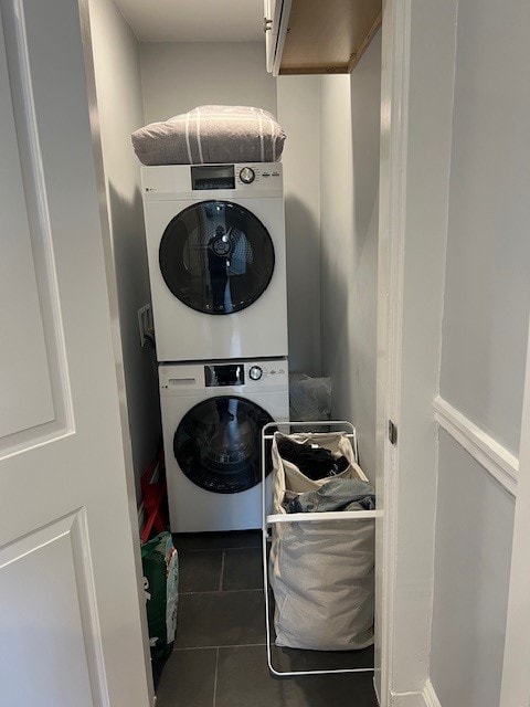 A compact laundry area is shown, featuring stacked washer and dryer units. A soft gray blanket rests atop the appliances. A laundry basket, along with a lightweight storage bin, is positioned beside the washer, while the walls are painted a neutral grey, enhancing the clean feel of the space.
