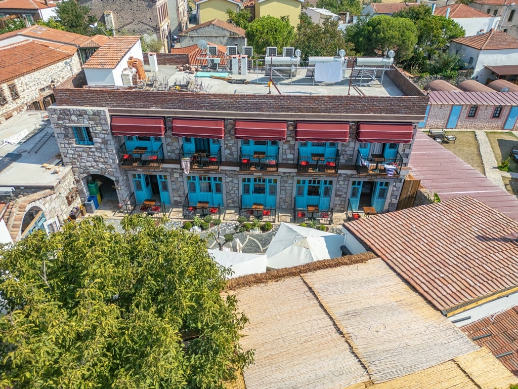 The exterior of a historic building is visible, featuring multiple balconies with red awnings. Bright blue doors are lined across the second floor, complementing the stone facade. A lush green tree partially frames the image, adding natural elements to the urban setting.