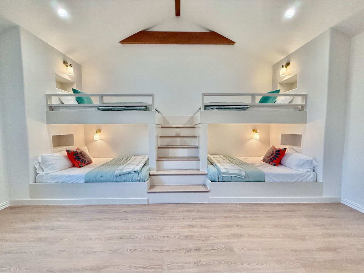 A dreamy guest bedroom with built-in bunk beds, offering two twin and two full beds adorned with light blue blankets and accented with playful pink throw pillows. Perfect for a cozy, stylish sleepover vibe!