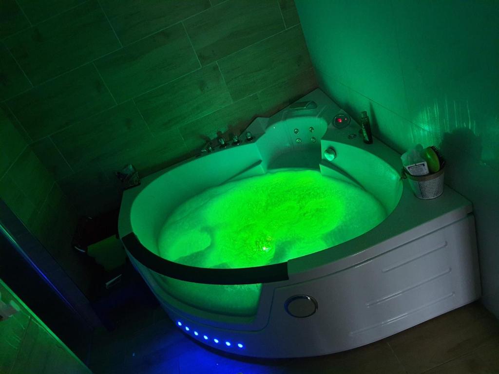 A spacious corner whirlpool tub is filled with bubbles and illuminated by soft green lighting. Surrounding walls feature a natural stone finish, while plumbing fixtures and bath accessories are neatly arranged nearby.