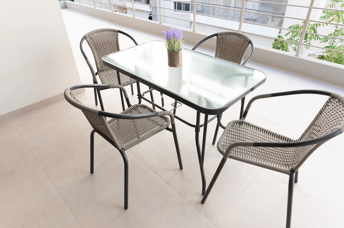 A dining table is positioned on the terrace, surrounded by four woven chairs. A small potted plant with lavender sits at the center of the table. The terrace features clean lines and a modern aesthetic, with a view of the surrounding greenery.
