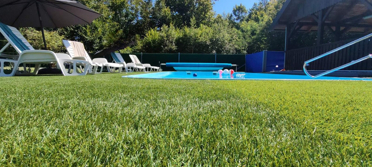 A well-maintained outdoor area features a sparkling blue pool surrounded by lush green grass. Poolside loungers are positioned under a shaded umbrella, providing a relaxing space for guests. Bright inflatable pool toys are visible in the water, enhancing the inviting atmosphere of outdoor leisure.