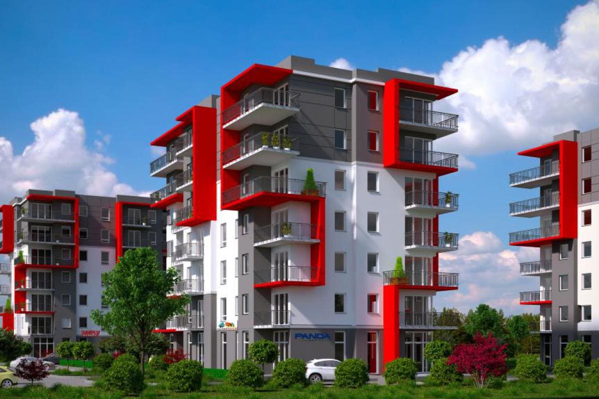 A modern apartment building features a striking combination of red and gray facades. Balconies extend from various floors, while landscaping with trees and shrubs enhances the exterior. The sky is clear with scattered clouds, providing a bright backdrop to the structure.