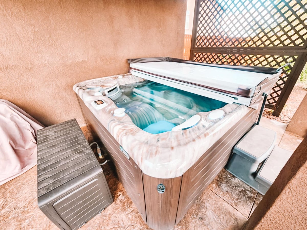 A private hot tub is positioned on a tiled area, covered partially by a protective enclosure. The tub features a smooth surface and is filled with water, reflecting soft light. A storage chest is nearby, adding convenience to the outdoor space.