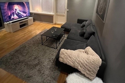 A spacious living area features a large sectional sofa adorned with soft cushions. A coffee table sits in front, accompanied by decorative items. A sizable television displays a fireplace scene, while textured rugs cover the wooden floor, creating a cozy ambiance.