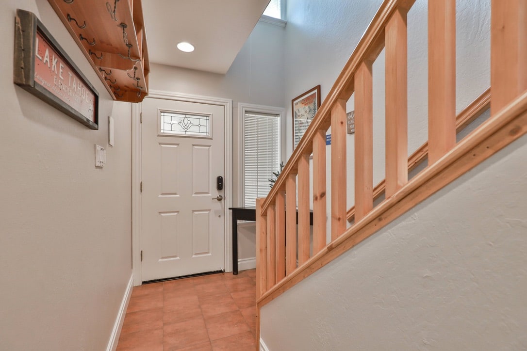 The entryway features ceramic tile flooring and a wooden staircase. A welcoming front door with decorative glass is prominently displayed, accompanied by wall decorations. Natural light is allowed in through a window above, enhancing the inviting atmosphere of the space.