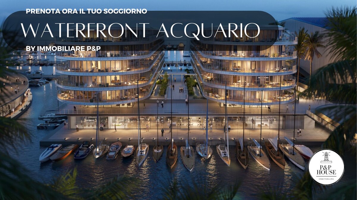 The Waterfront Acquario residence is displayed with a contemporary architectural design, featuring multiple levels of sleek, curved balconies. A marina is visible below, with various boats docked along the waterfront, framed by palm trees and a serene evening sky.