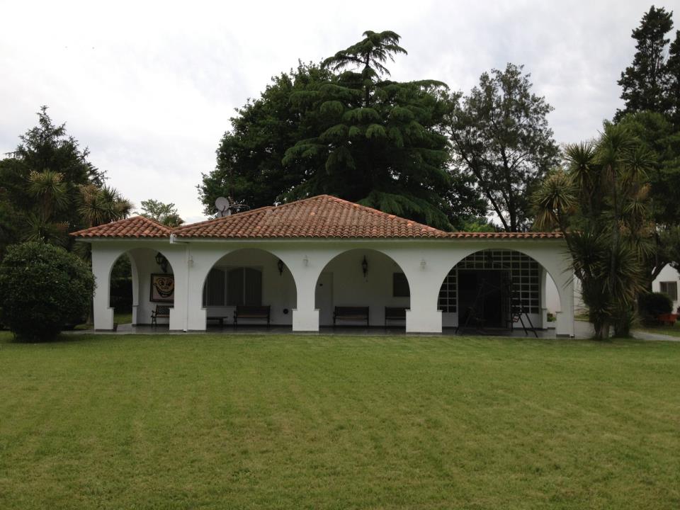 A single-story structure features a red-tiled roof and arched openings that provide a shaded walkway. A well-maintained lawn surrounds the building, which is complemented by ornamental shrubs and trees that offer greenery.
