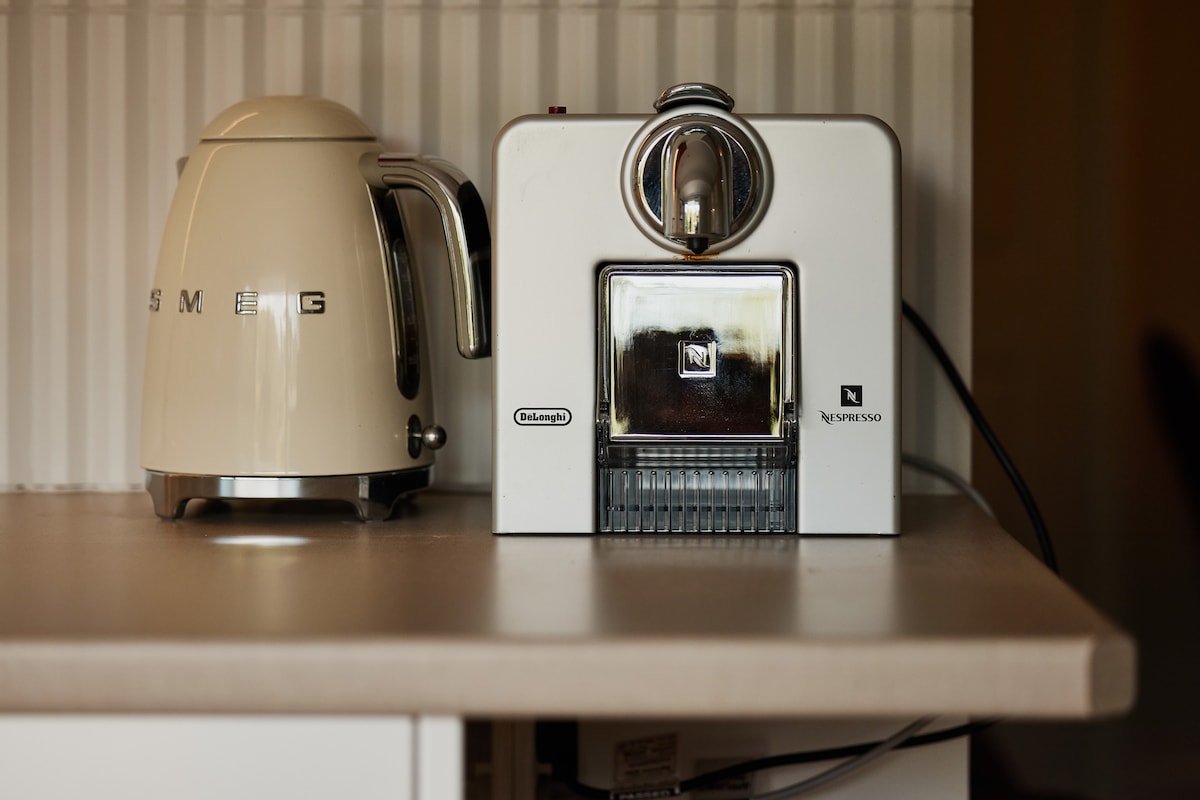 A modern kitchen countertop features a sleek Nespresso machine alongside a stylish kettle. The appliances are housed against a textured wall, enhancing the overall contemporary design of the space.