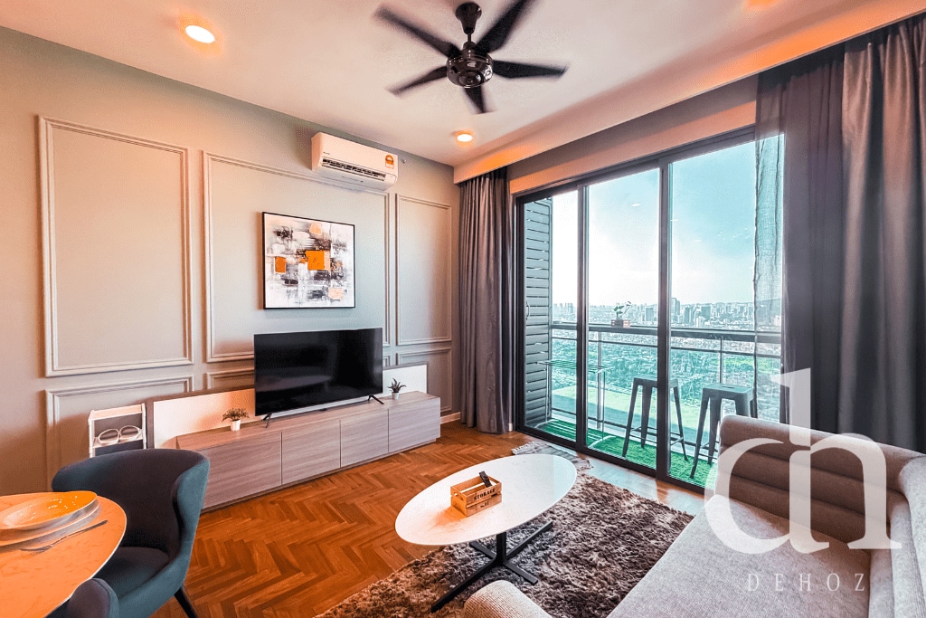 A contemporary living space features a sleek television mounted on a light wooden cabinet. Large glass doors open to a city view, allowing natural light to illuminate the room. A circular coffee table is centrally placed, and neutral tones are complemented by artistic wall décor.