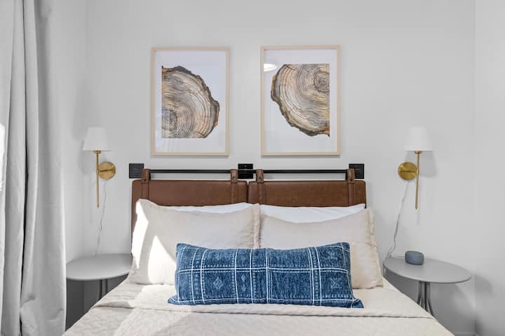 Cama tamaño queen con lámparas de noche, mesitas y reloj despertador con máquina de sonido.