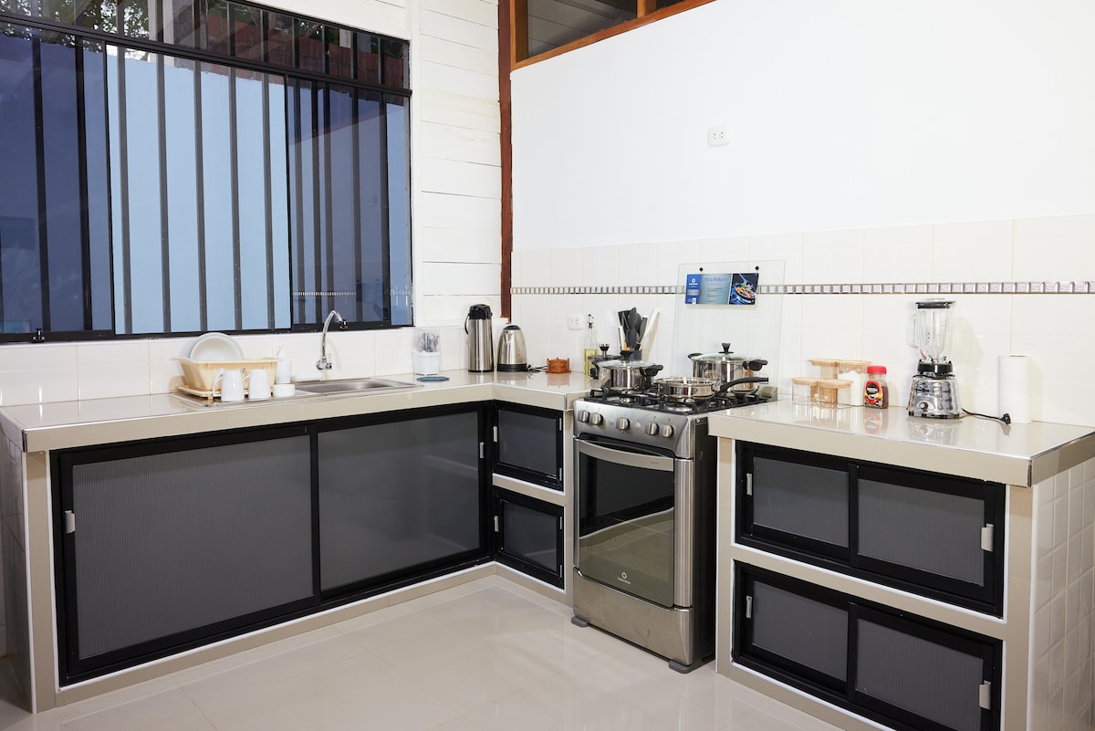 A modern kitchen features sleek countertops and a stainless steel gas stove. Ample cabinetry provides storage, while a large window allows natural light to fill the space. A variety of kitchen appliances, including a kettle and coffee maker, are neatly arranged for convenience.