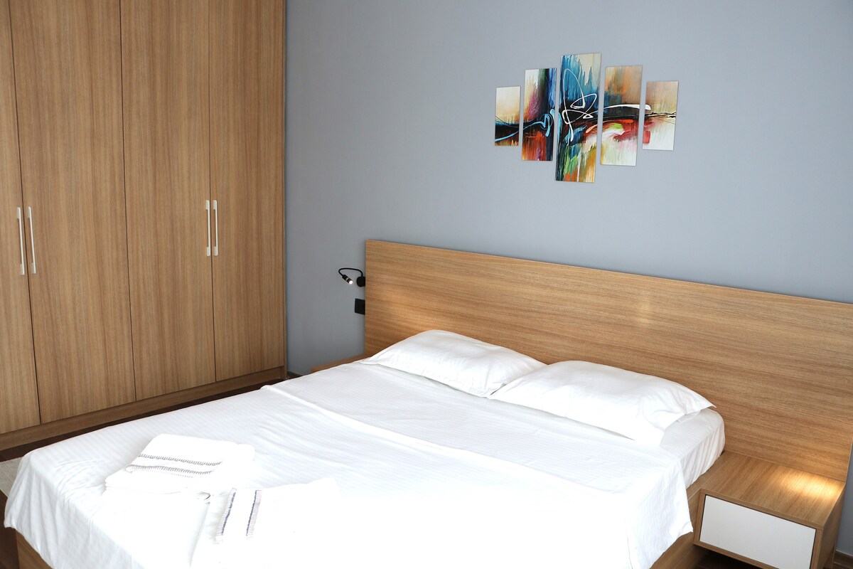 นี่เป็นห้องนอนที่ทันสมัยพร้อมเตียงขนาดใหญ่และตู้เสื้อผ้าขนาดใหญ่ ผนังทาสีด้วยสีเงินอ่อน มีมุมแต่งหน้าพร้อมกระจกและพื้นที่เก็บของ ห้องนอนมีแสงสว่างเพียงพอและยังมีผ้าม่านเพื่อทำให้ห้องมืดลง