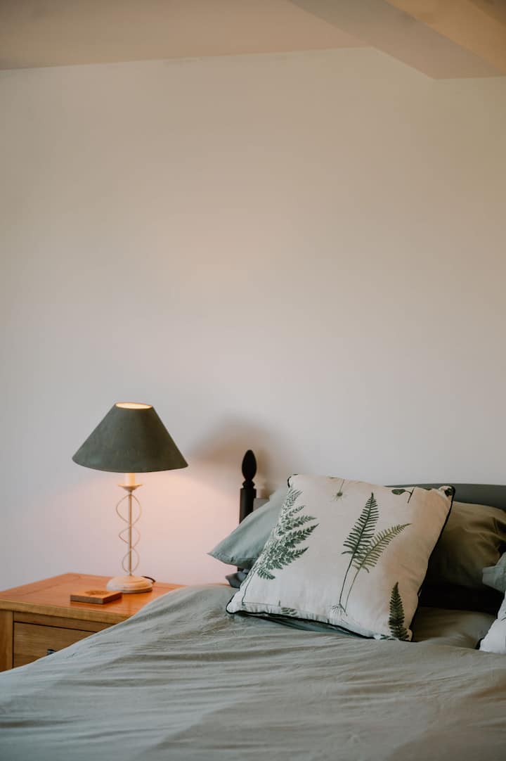Cama doble con cojines acogedores e iluminación suave junto a la cama.