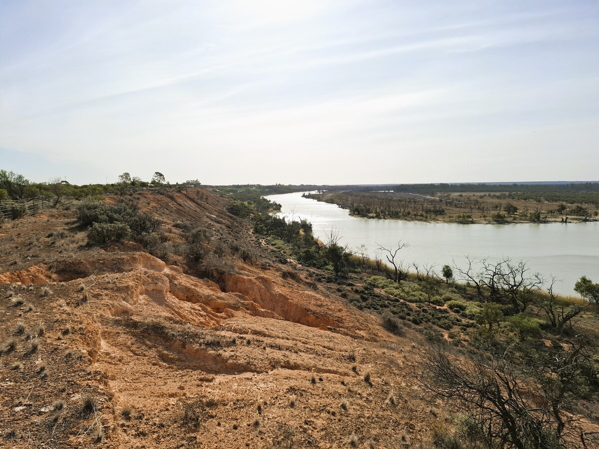 A scenic view of the Pike River meanders through the landscape, framed by gentle slopes and sparse vegetation. The tranquil waters reflect the soft light of the sky, while the surrounding hills contribute to the natural beauty of the Riverland South Australia.