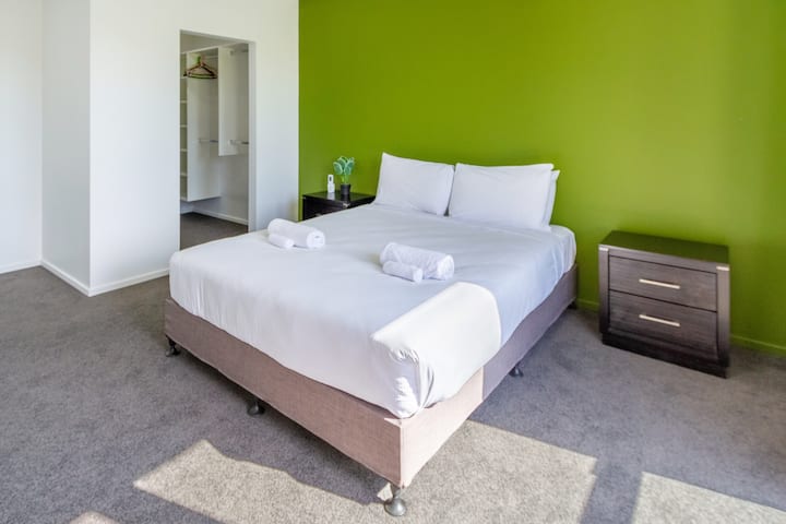 moderná a čistá spálňa so zelenou zvýraznenou stenou s dekoratívnymi odkladacími stolíkmi