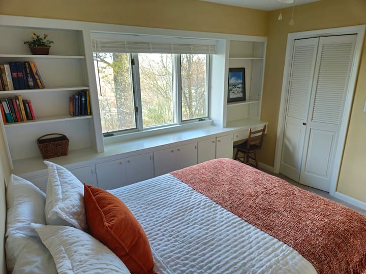 Spavaća soba s bračnim krevetom i ugrađenom policom za knjige/radni stol, stropnim ventilatorom, ormarima i prelijepim pogledom na planine.