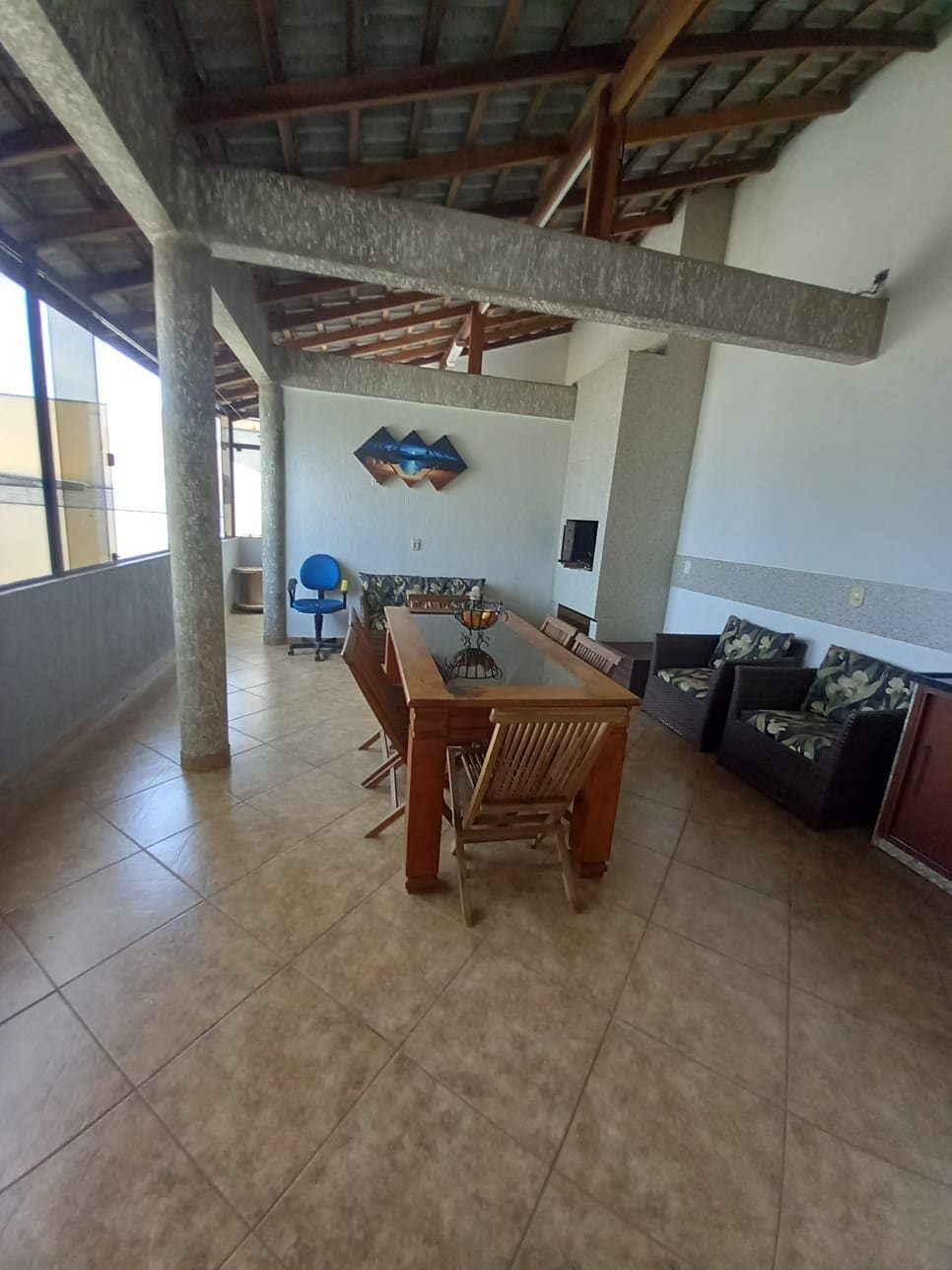 A spacious living area is depicted, featuring a wooden dining table surrounded by woven chairs. Comfortable seating in the form of two armchairs with floral cushions is visible. Large windows allow natural light to illuminate the room, with a television mounted on the wall.