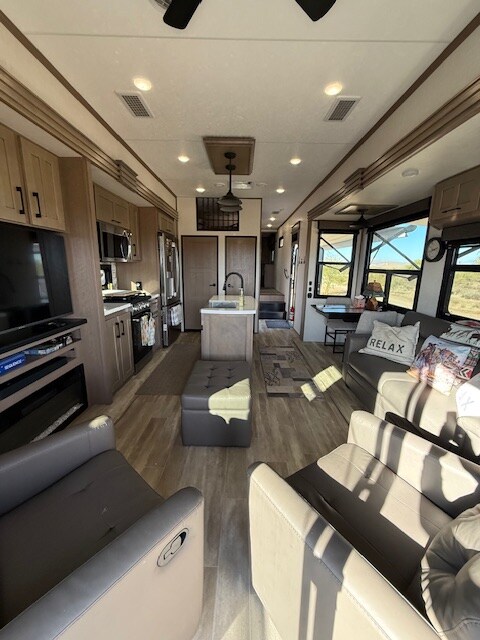 A modern interior showcases an open living space with light-colored cabinetry and a central kitchen island. Comfortable seating options are arranged around a spacious lounge area. Large windows offer views of the surrounding landscape, and natural light fills the room.