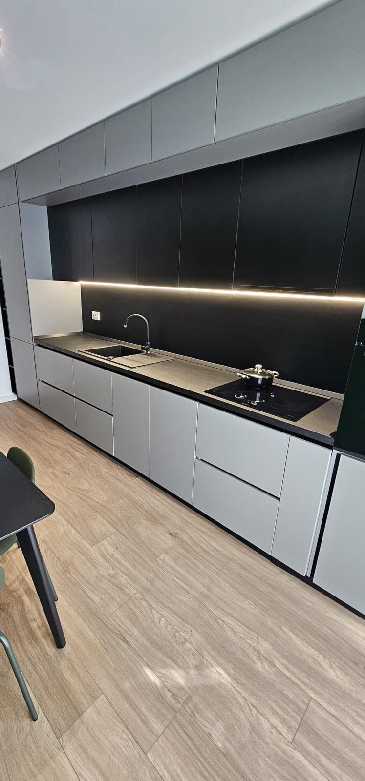 A modern kitchen is displayed with sleek black cabinetry and contrasting light countertops. Integrated appliances are visible, along with a minimalist sink and faucet. Soft lighting highlights the workspace, creating a functional and visually appealing cooking area.