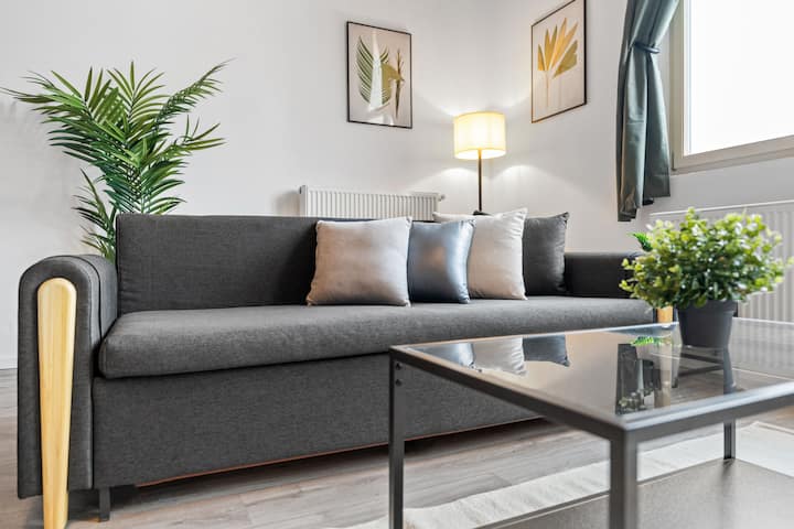 Sofa ya starehe sebuleni inakualika upumzike, ukiwa umezungukwa na mito maridadi na mwangaza wa upole. Inafaa kwa jioni ya kupumzika yenye kitabu au filamu katika mazingira ya kisasa, tulivu.