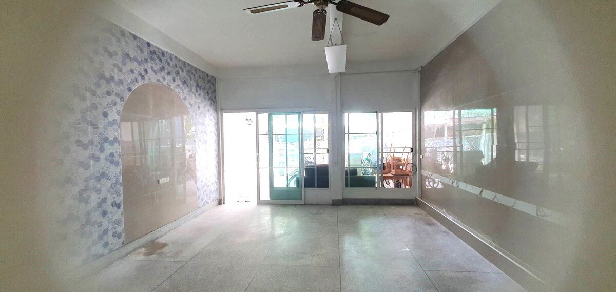 An open living space features a ceiling fan and large sliding glass doors offering access to an outdoor area. One wall showcases a decorative blue pattern, while smooth, light-colored flooring extends throughout the room, creating a clean and spacious environment.