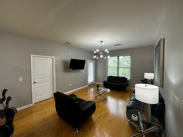 A spacious living area features a modern design with hardwood flooring. Two black leather sofas are arranged opposite a glass coffee table. A sleek lamp provides soft lighting beside the window, which allows natural light to illuminate the room. A mounted TV is visible on the wall.