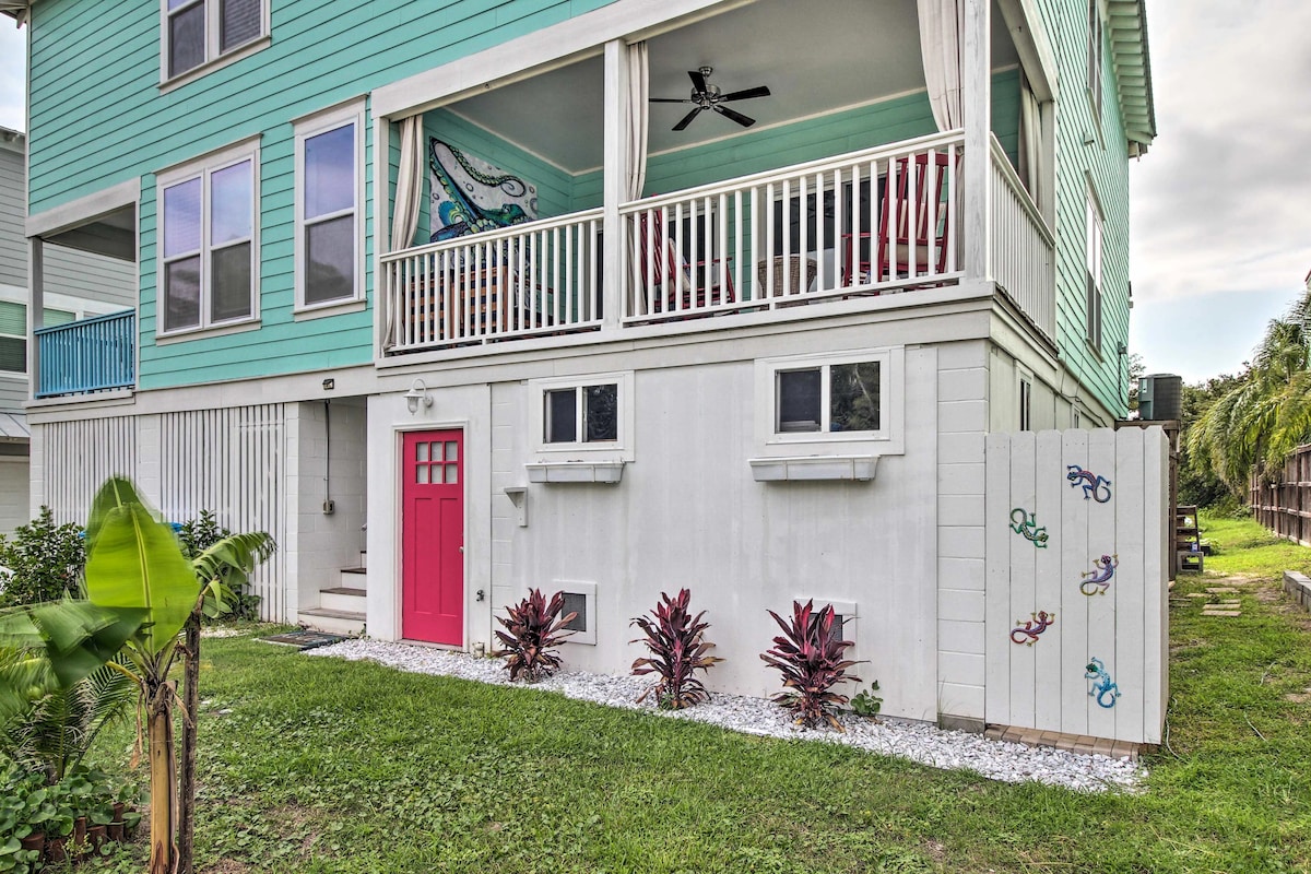 The exterior of the townhome features a vibrant turquoise facade complemented by a bright pink door. A spacious porch is adorned with comfortable seating and a ceiling fan. Lush green landscaping surrounds the property, enhancing its welcoming appearance.