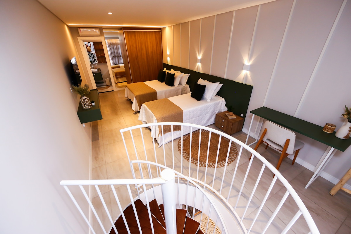An open and airy space is highlighted, featuring two beds arranged in a bright room. Soft lighting from wall-mounted fixtures enhances the inviting ambiance. A spiral staircase leads to the upper level, while a neutral color palette creates a calming atmosphere.
