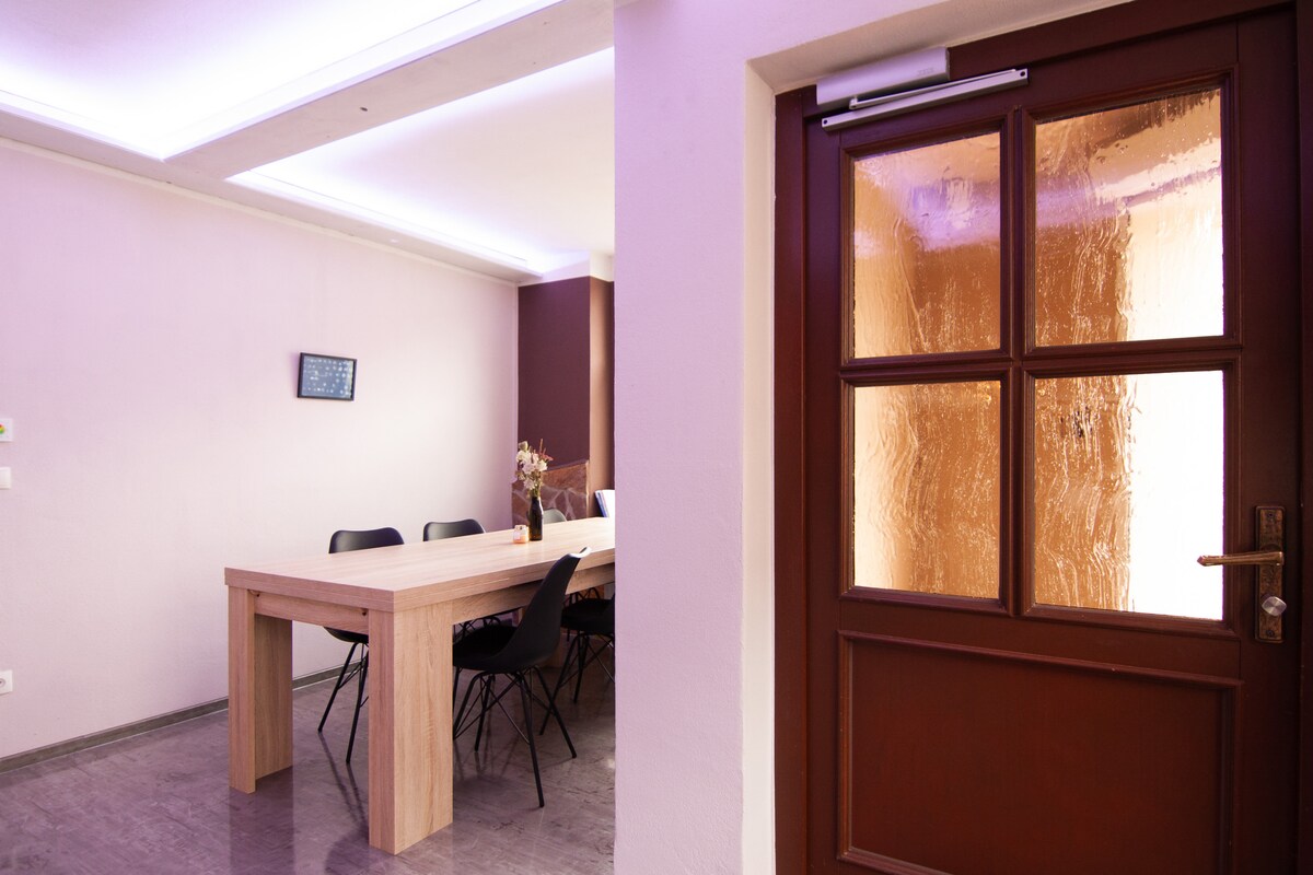 An inviting entrance leads to a spacious dining area, where a long wooden table is surrounded by black chairs. Soft lighting casts a warm glow on the features, enhancing the modern aesthetic. A frosted glass door adds texture to the entryway.