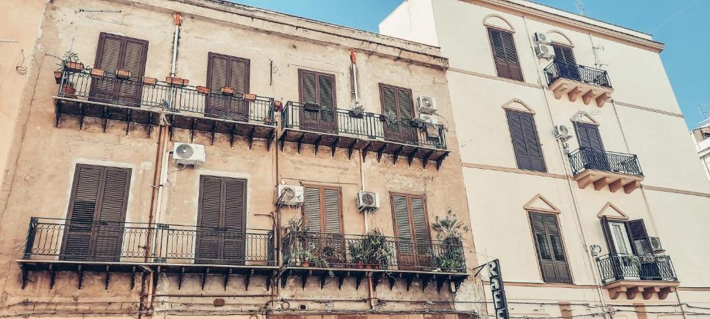 The image captures a charming facade with two multi-story buildings. The balconies feature potted plants and air conditioning units, while wooden shutters frame each window. The warm tones of the walls are contrasted by the clear blue sky above.