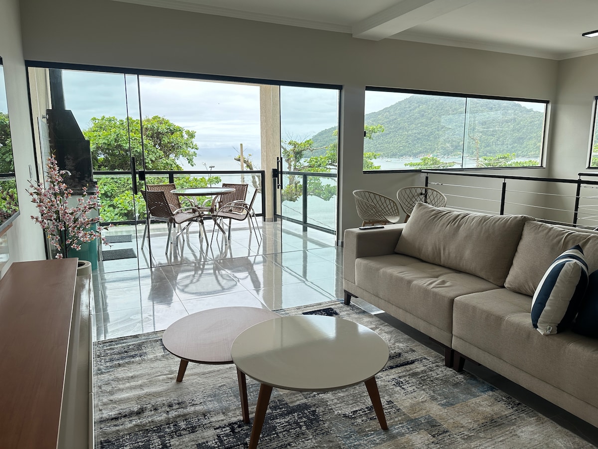 A modern living area features large glass doors that open to a spacious balcony with ocean views. A comfortable sofa and a round coffee table are present, along with a dining set for four, creating a serene space for relaxation.