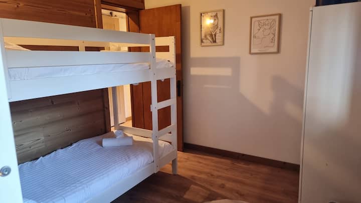 غرفة دافئة مع سريرين أبيضين بطابقين، مثالية لحظات الاسترخاء للعائلات أو مجموعات الأصدقاء. مسكن مريح ومريح ومثالي للإقامة في قلب الطبيعة.